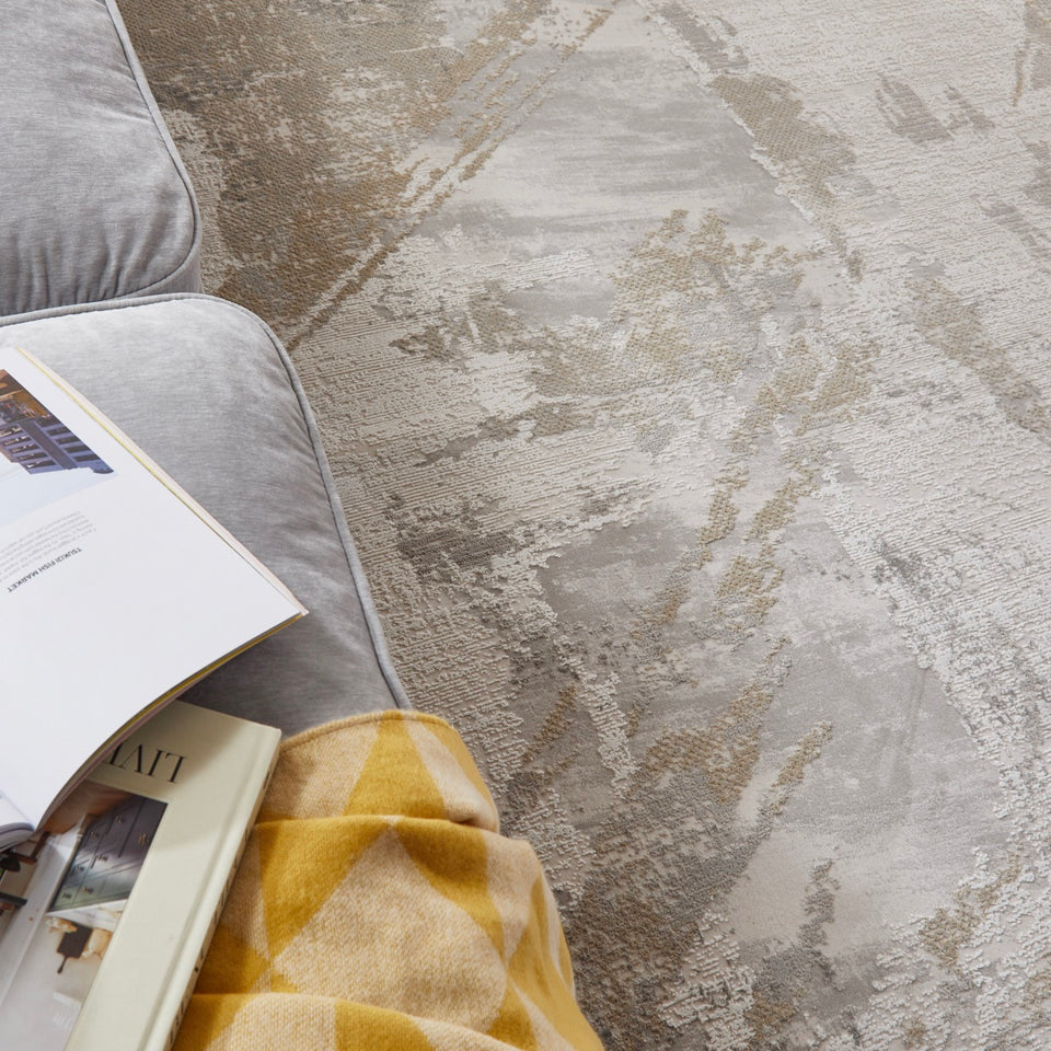 Textured rug with a pattern, part of a sofa and books on a table.